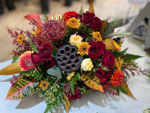 Mixed bouquet with red roses, yellow daisies, and tropical foliage