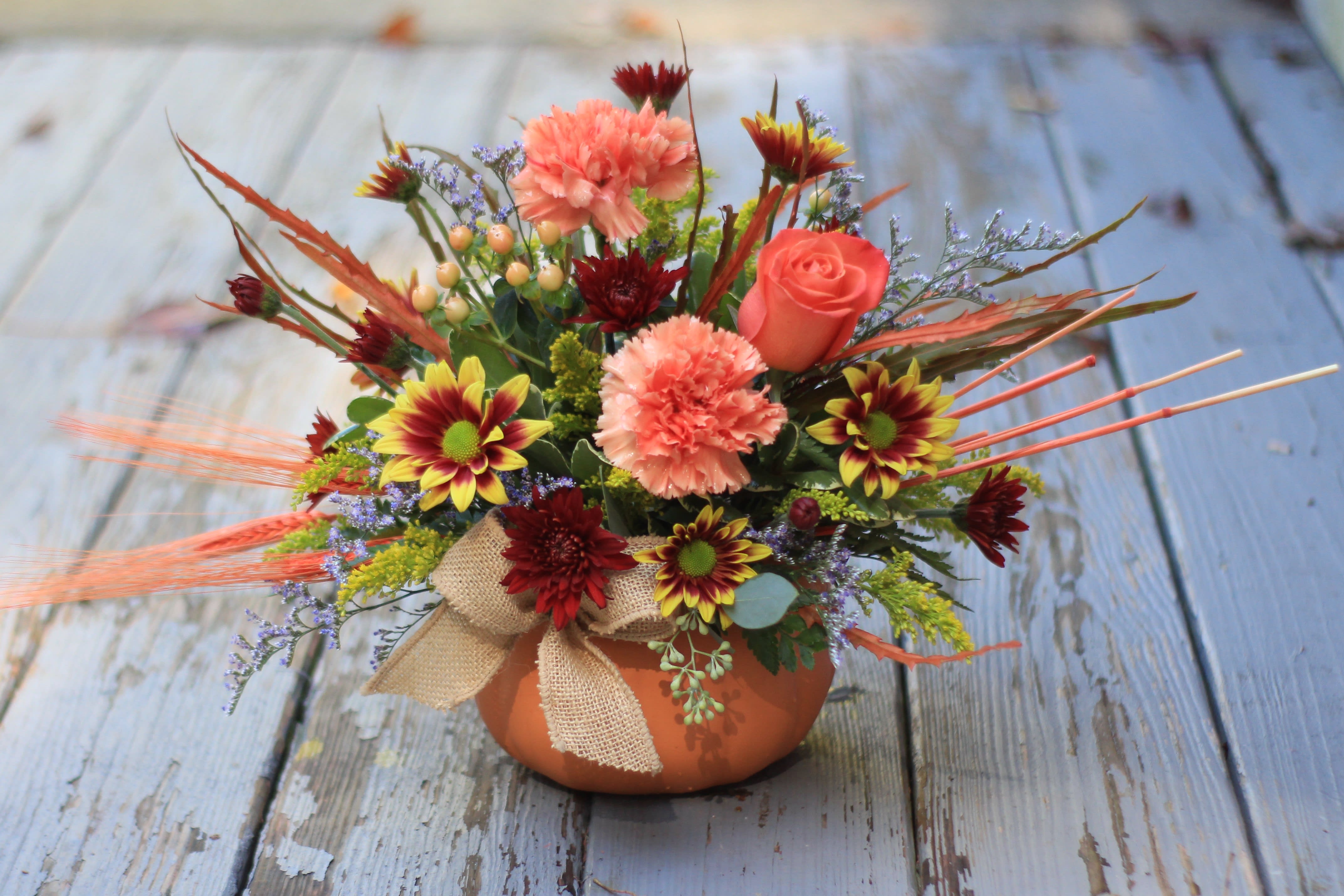 Colorful floral arrangement in a small orange pot with a burlap bow