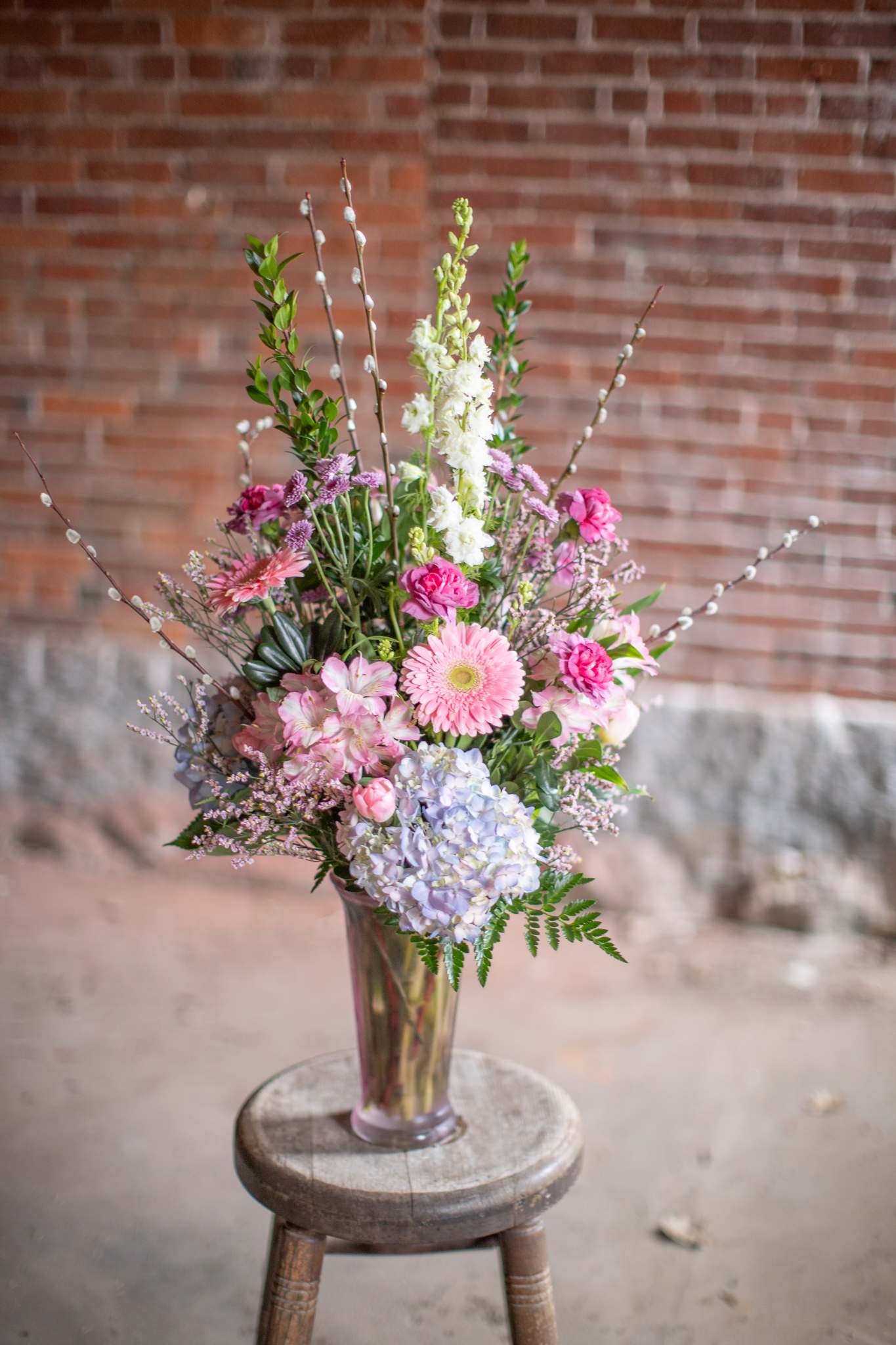 Tall pastel bouquet in a clear glass vase on a stool
