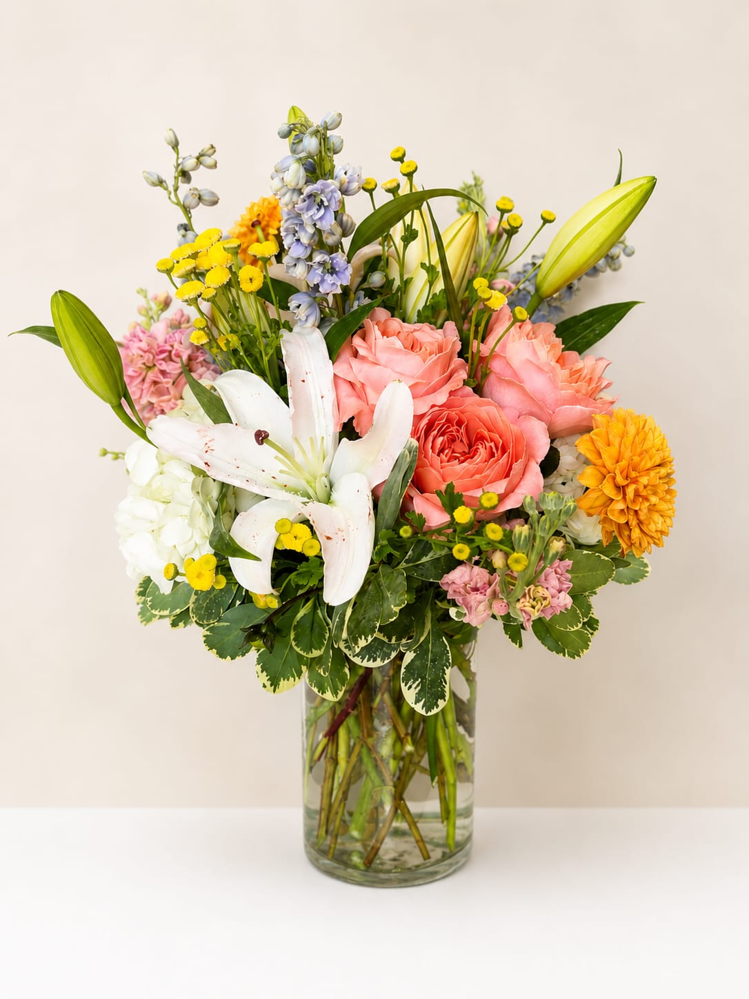 Bright Side - Featuring a beautiful blend of coral, creamy white, soft blues, and pops of yellow blooms artfully arranged in a clear glass vase. With it's garden-inspired style and graceful texture, this arrangement is perfect for celebrating life's special moments, making someone's day a little brighter, or simply expressing love. Please note, flowers are a natural product and natural variations do occur. Flower varieties may very depending on seasonal availability while maintaining the overall color palette and style.