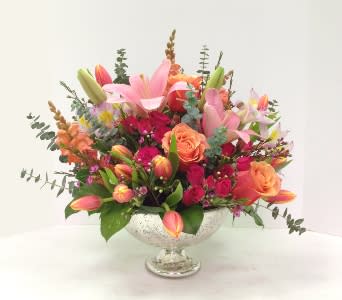Mixed pink, orange, and yellow flowers in a clear pedestal bowl