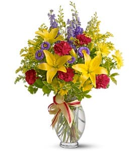 Bouquet of yellow lilies, red carnations, and purple flowers in a glass vase