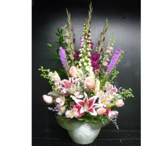 Tall pink and purple mixed flower arrangement with lilies and roses in a white ceramic vase