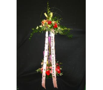 Tall two-tiered standing floral spray with red flowers and printed ribbons on a black background