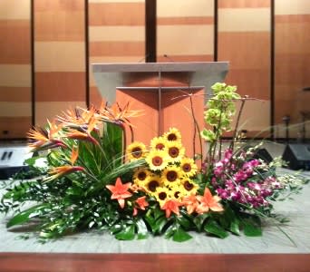 Large stage arrangement with birds of paradise, sunflowers, lilies, and orchids in front of a podium