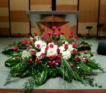 Large red rose and white flower spray with abundant foliage arranged in front of a podium
