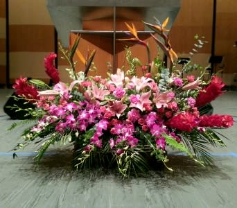 Large pink and red tropical altar spray with lilies and orchids arranged low and wide on a stage
