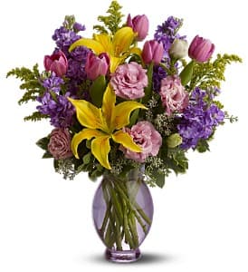 Bouquet of yellow lilies, pink tulips, and purple flowers in a glass vase