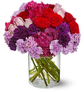 Bouquet of red roses and pink-purple carnations in a clear glass vase