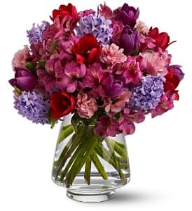 Mixed pink, purple, and red flowers in a clear glass vase