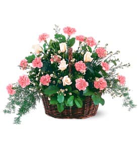 Basket arrangement of pink carnations, pale roses, and trailing greenery.