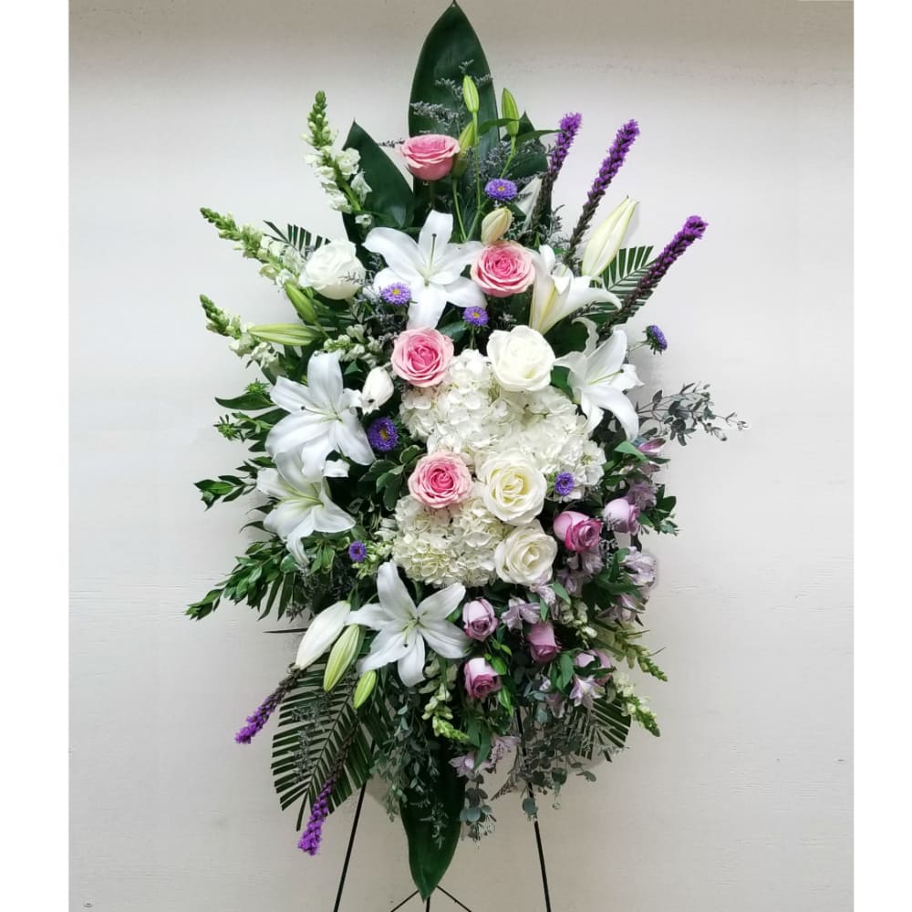 Tall standing spray of white lilies, hydrangeas, and pink roses with purple accents on an easel