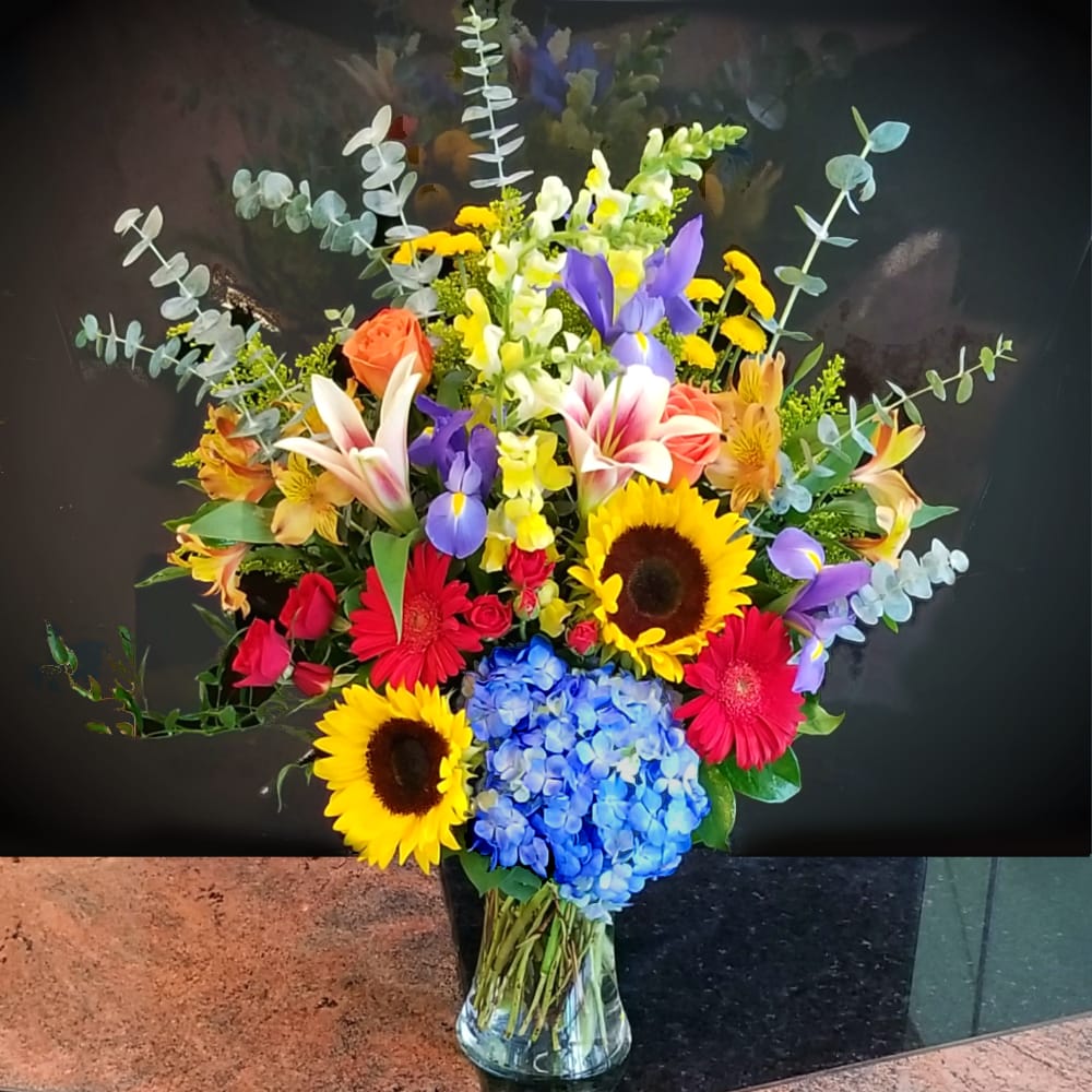 Colorful mixed bouquet with sunflowers, lilies, roses, and hydrangea in a glass vase