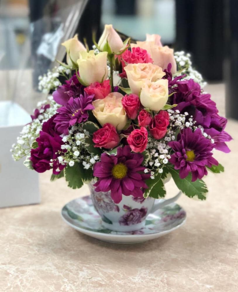 Bouquet of pink and cream roses with purple daisies in a floral teacup