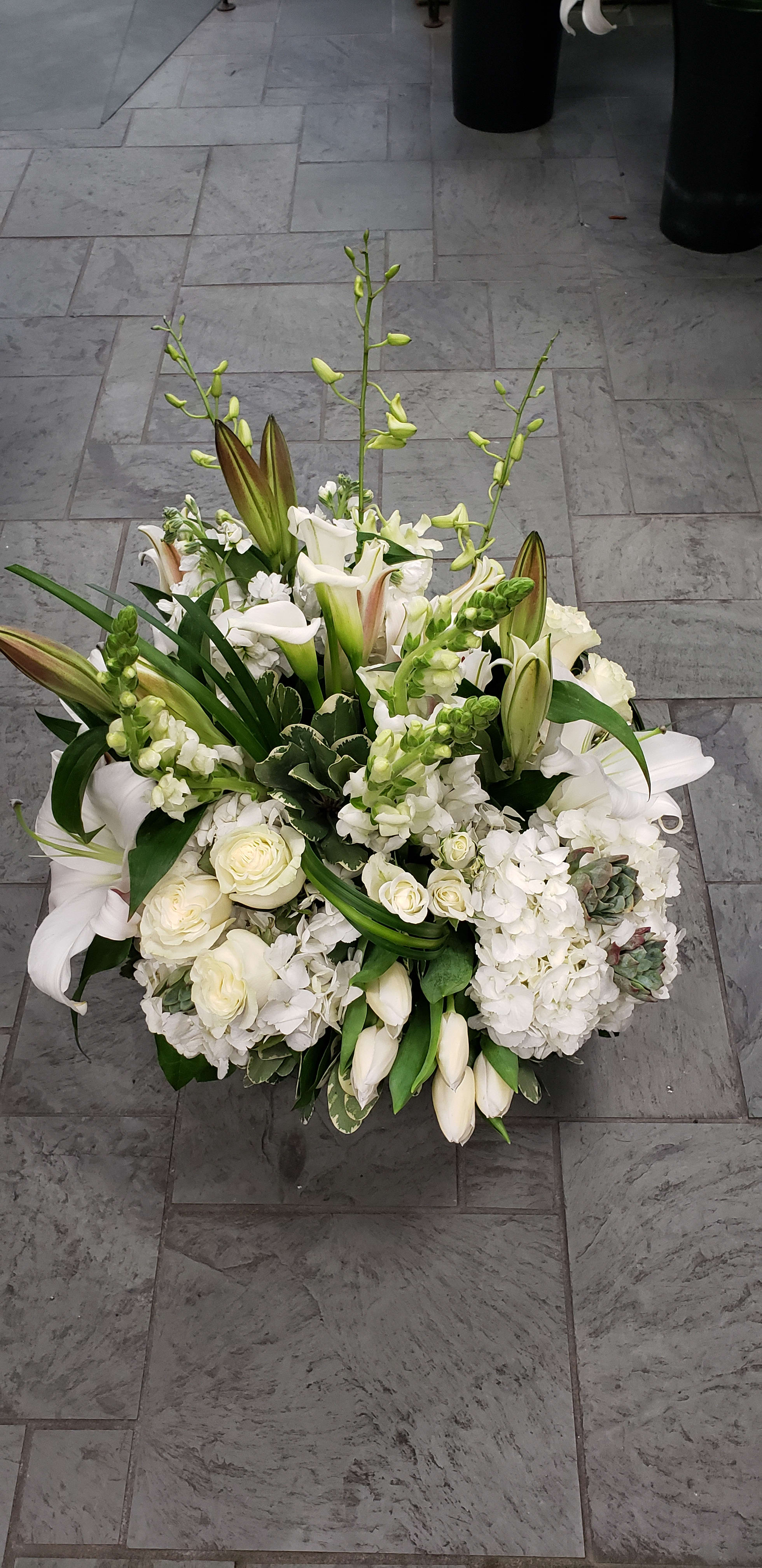 White floral arrangement with lilies, roses, and calla lilies in a low design