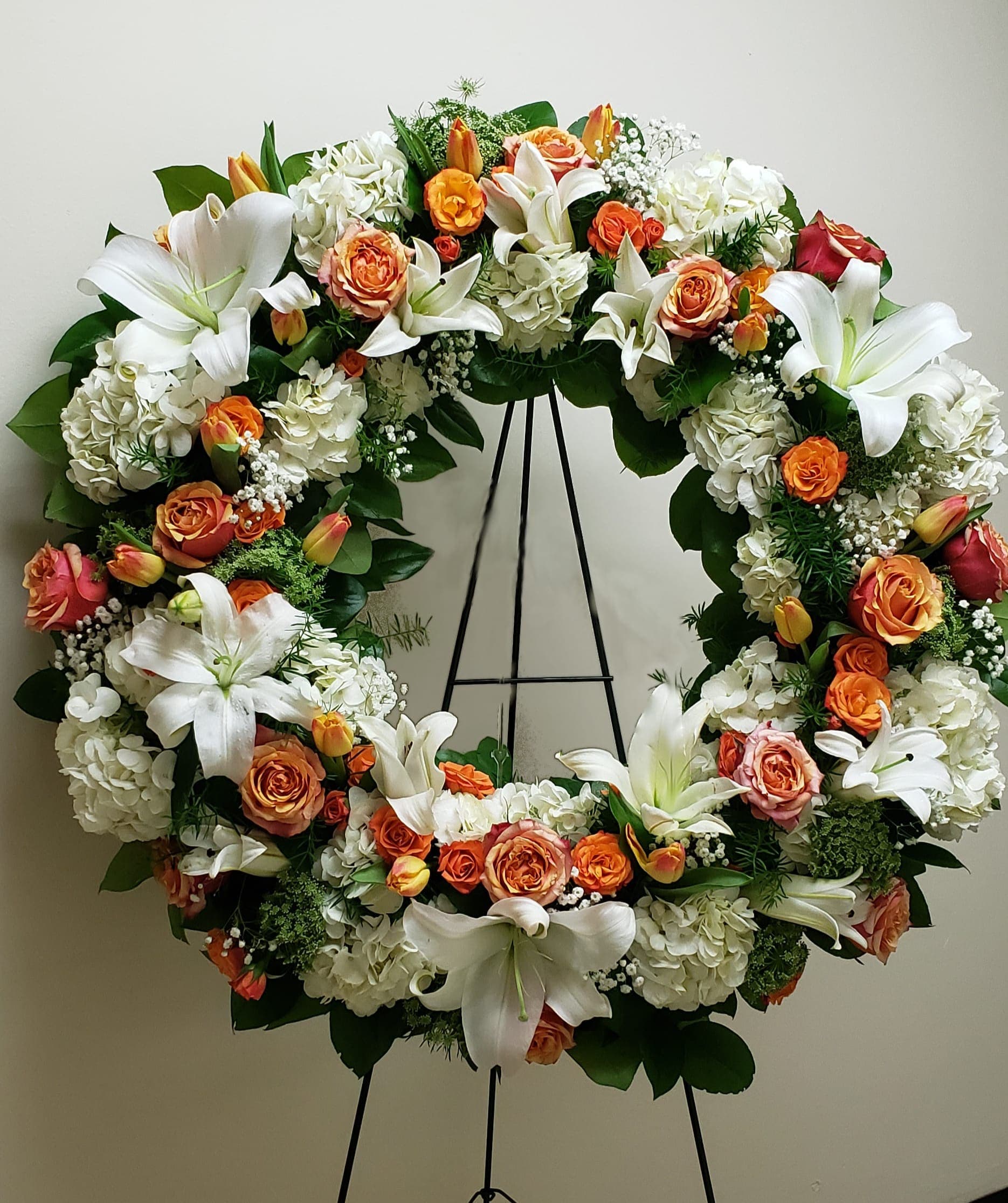 Standing wreath of white lilies, hydrangeas, and orange roses on a metal easel