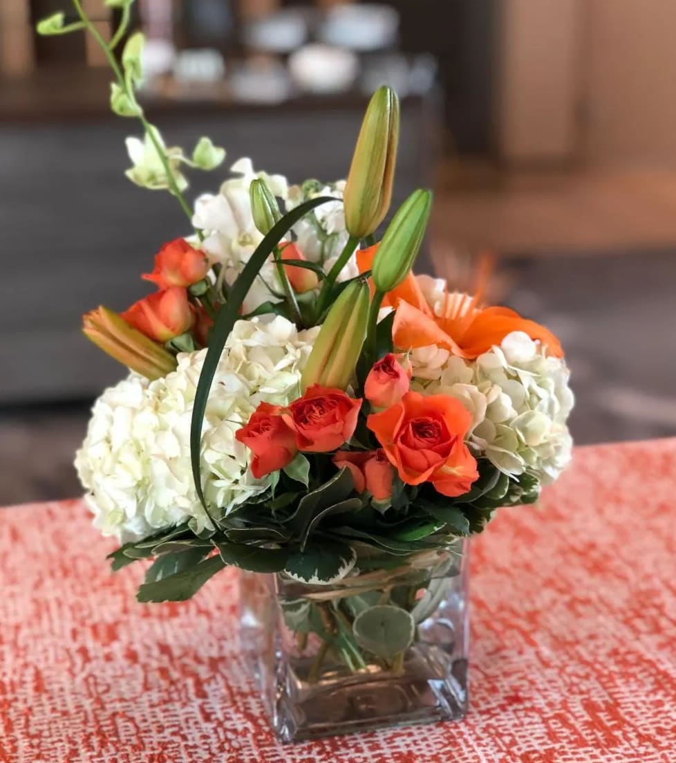Orange roses and white hydrangeas in a square glass vase