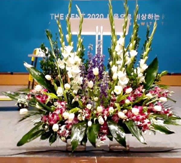 Large stage arrangement with white spikes, purple flowers, and pink orchids in a wide fan shape