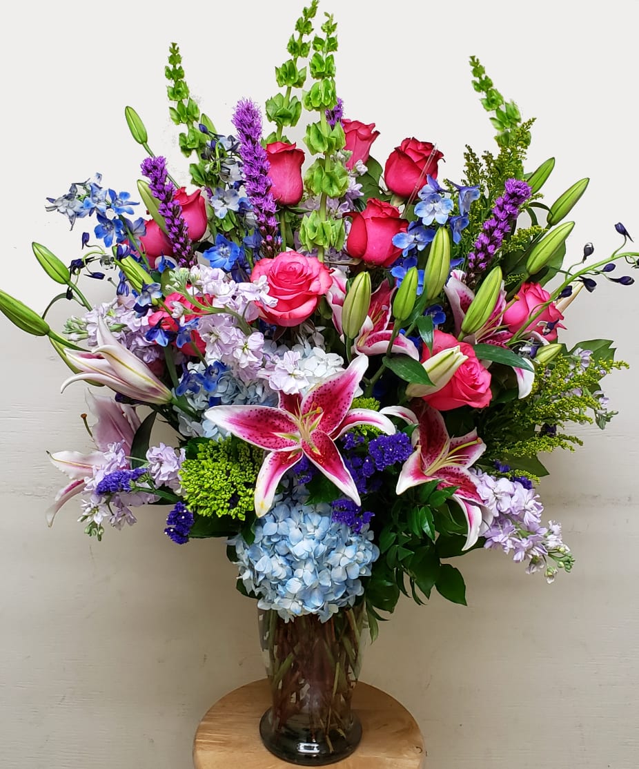 Large mixed bouquet with pink roses, lilies, and blue flowers in a glass vase