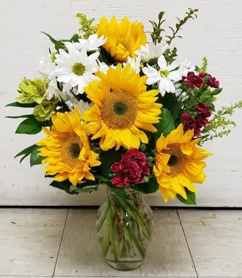 Bouquet of sunflowers, white daisies, and red flowers in a glass vase