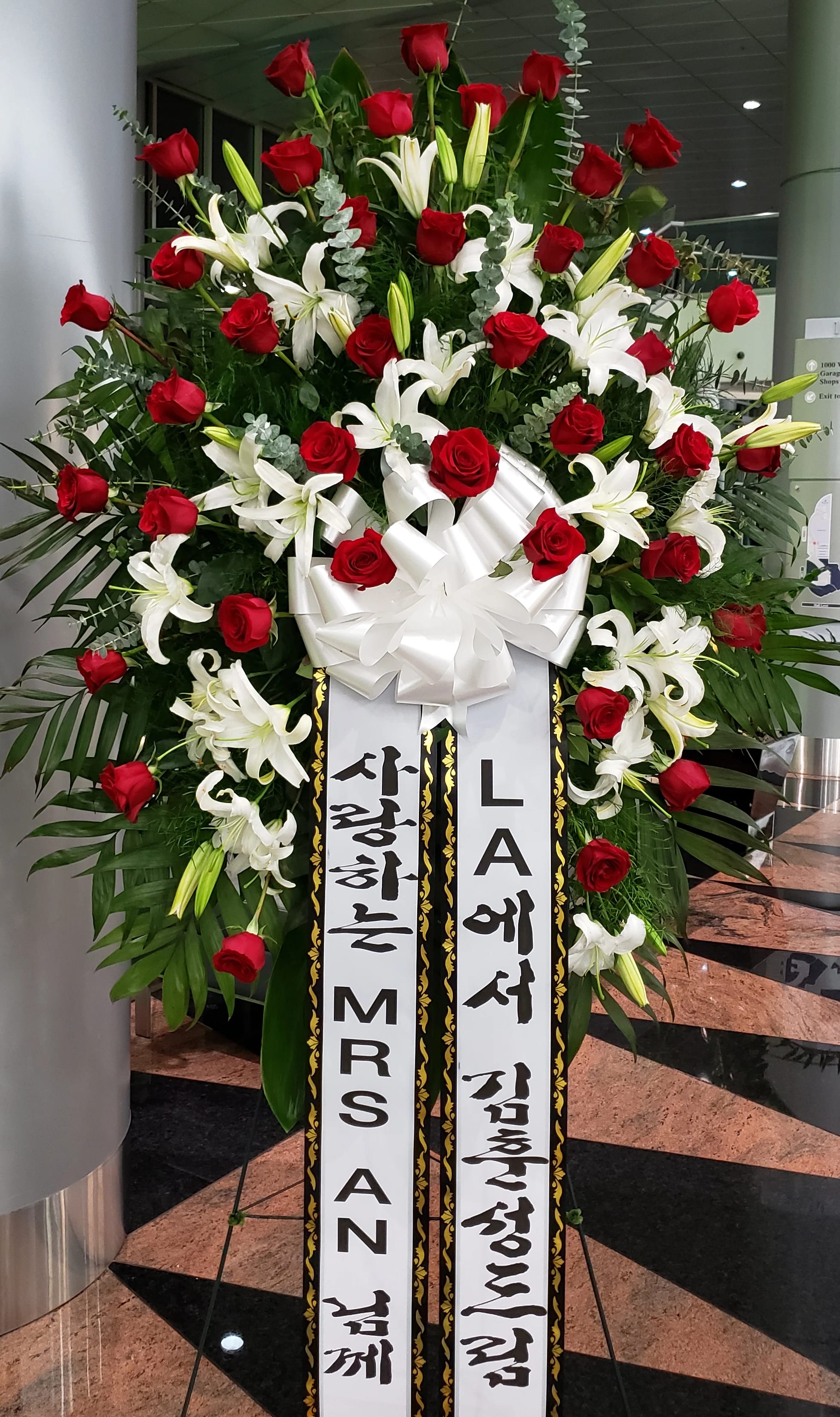 Large standing floral spray with red roses and white lilies, topped with a white bow