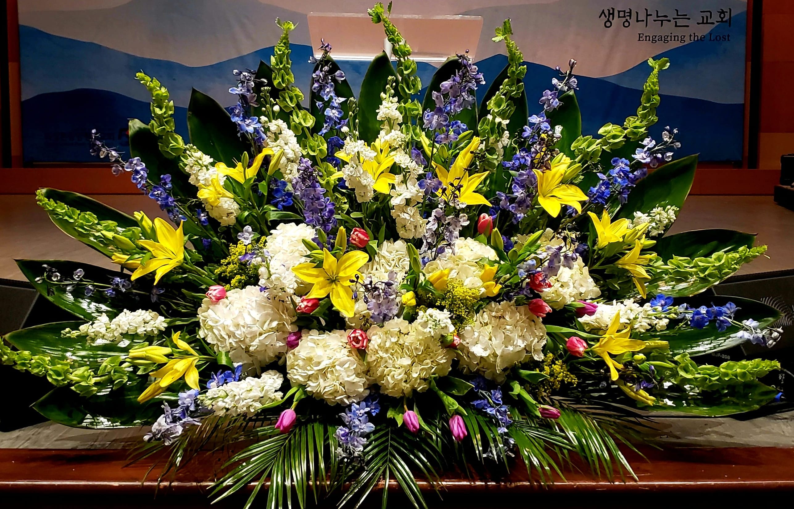Large altar arrangement of yellow lilies, white hydrangeas and blue flowers in a fan-shaped display