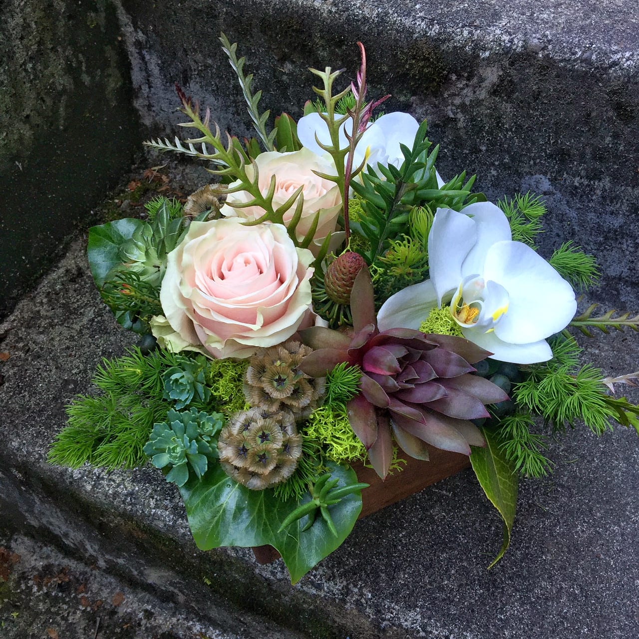 Arrangement of pale pink roses and white orchids with succulents