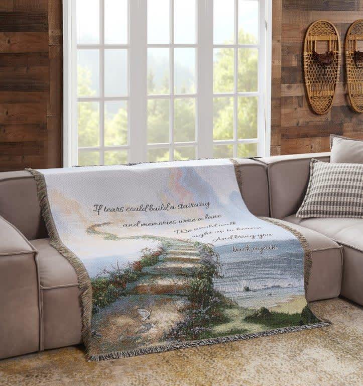 A decorative throw blanket with a seaside staircase scene and cursive text draped over a sofa