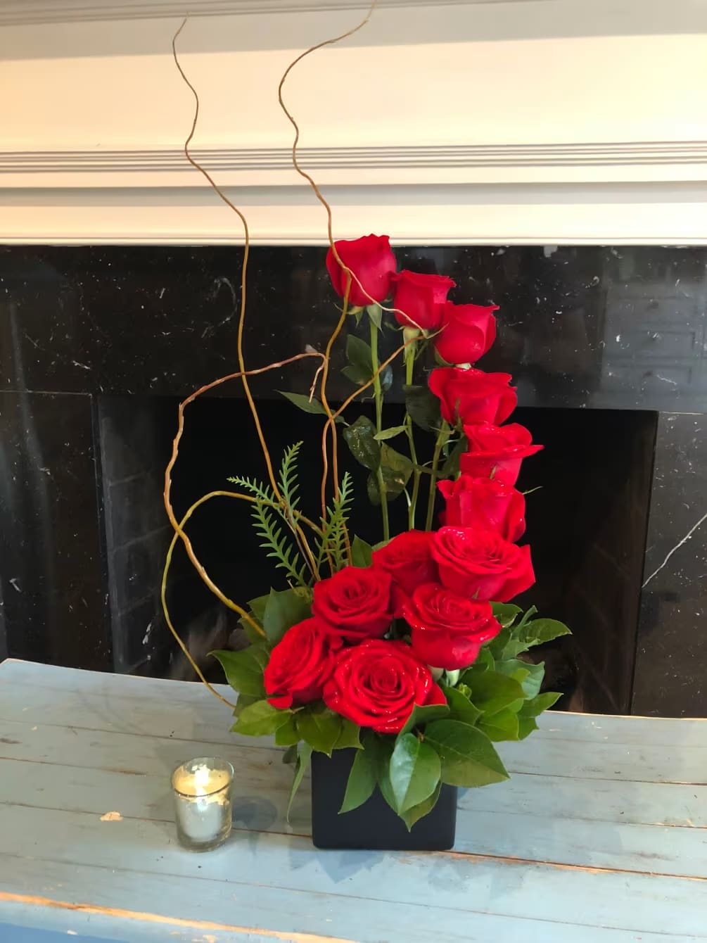 Red roses arranged in a tall black vase with curly branches