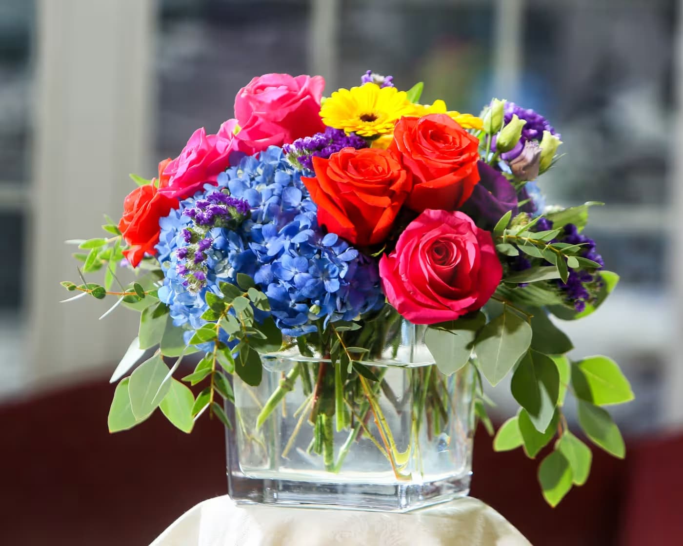 Colorful bouquet of roses, hydrangeas, and a yellow daisy in a glass vase