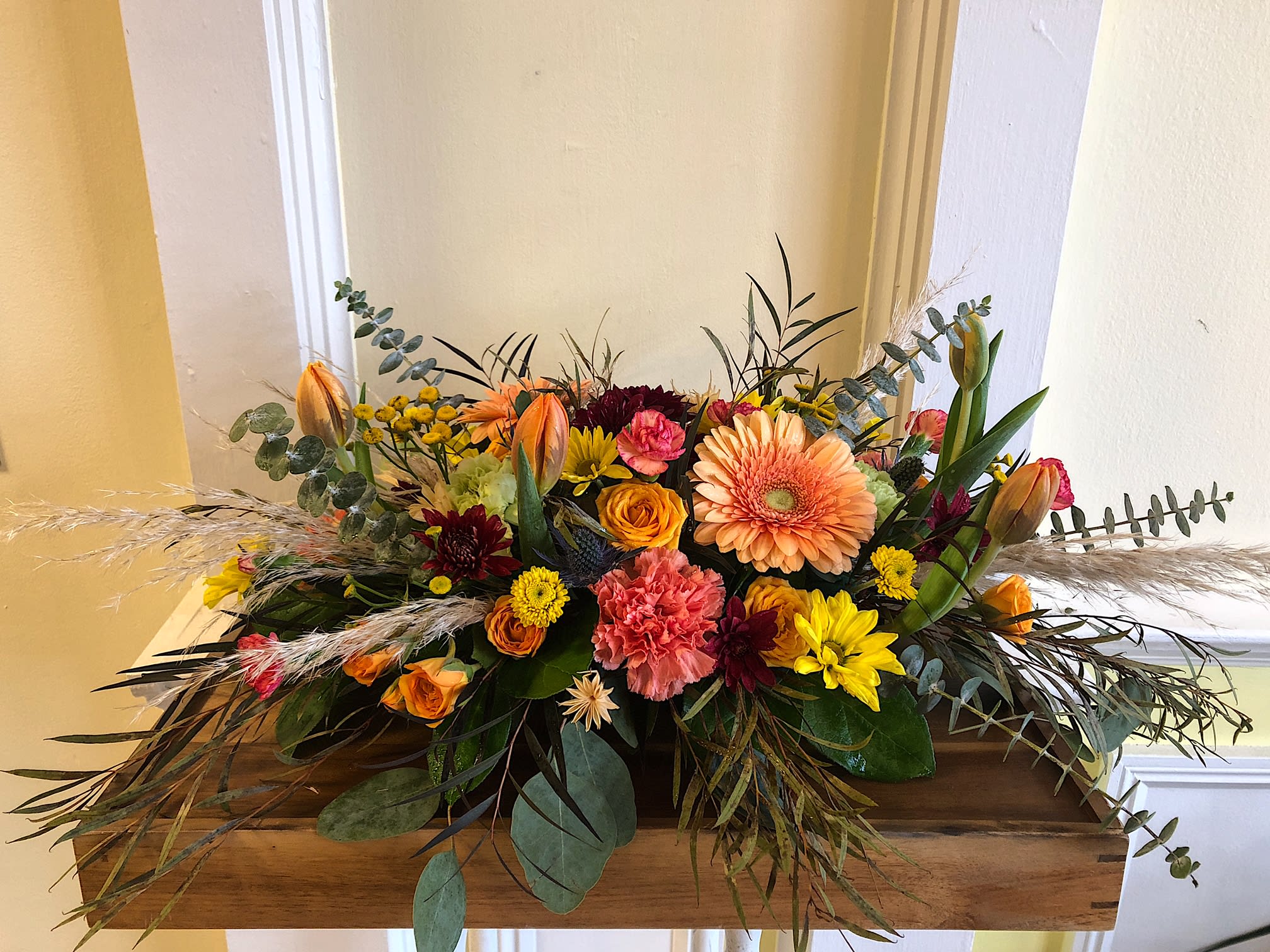 Low floral arrangement with orange, yellow, pink, and burgundy blooms