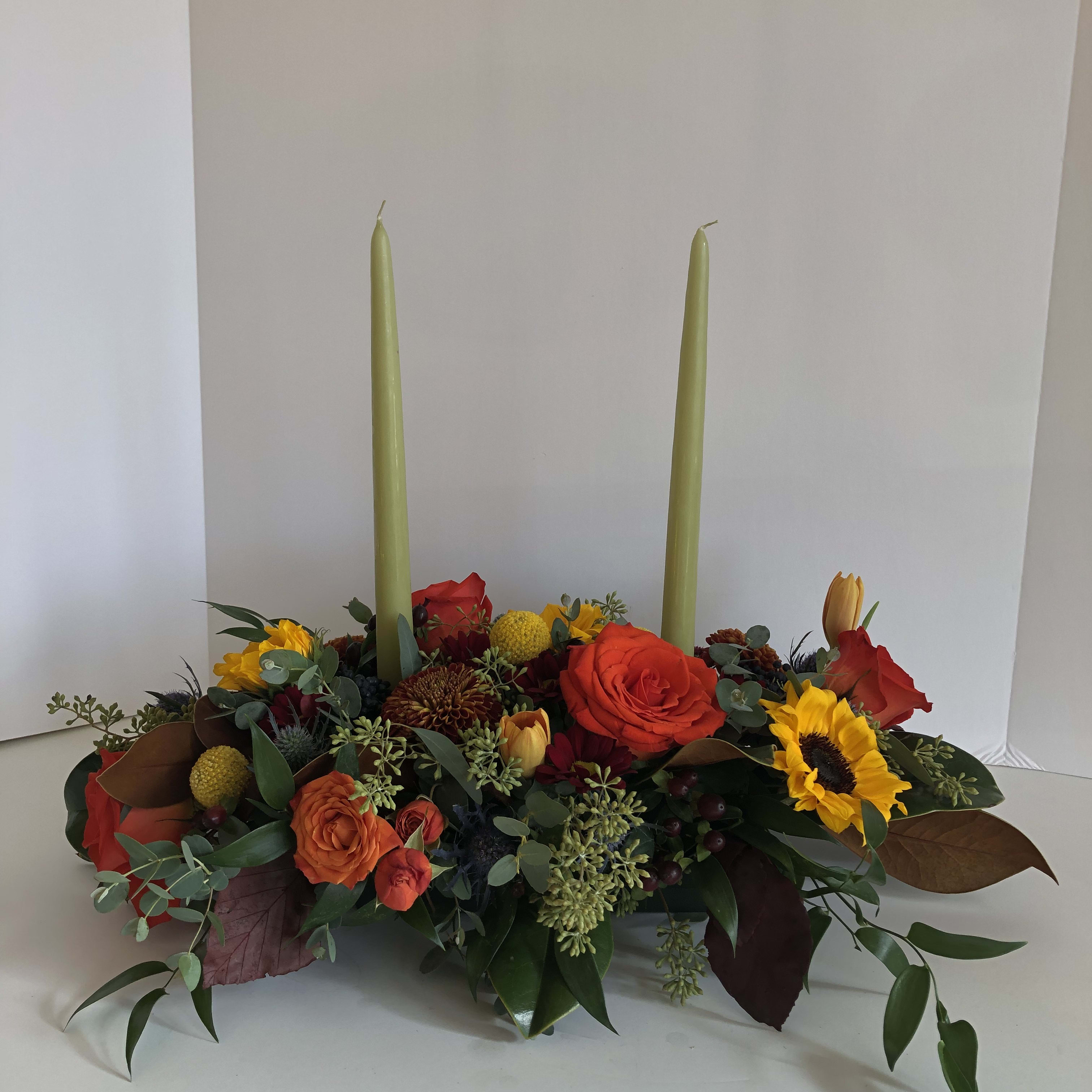 Low floral centerpiece with two tall candles and bright mixed blooms