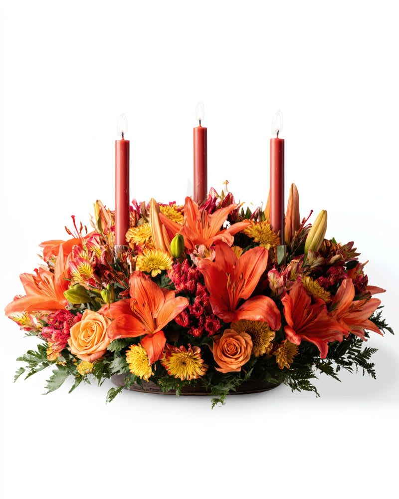 Low floral centerpiece with orange lilies, roses, and three red taper candles
