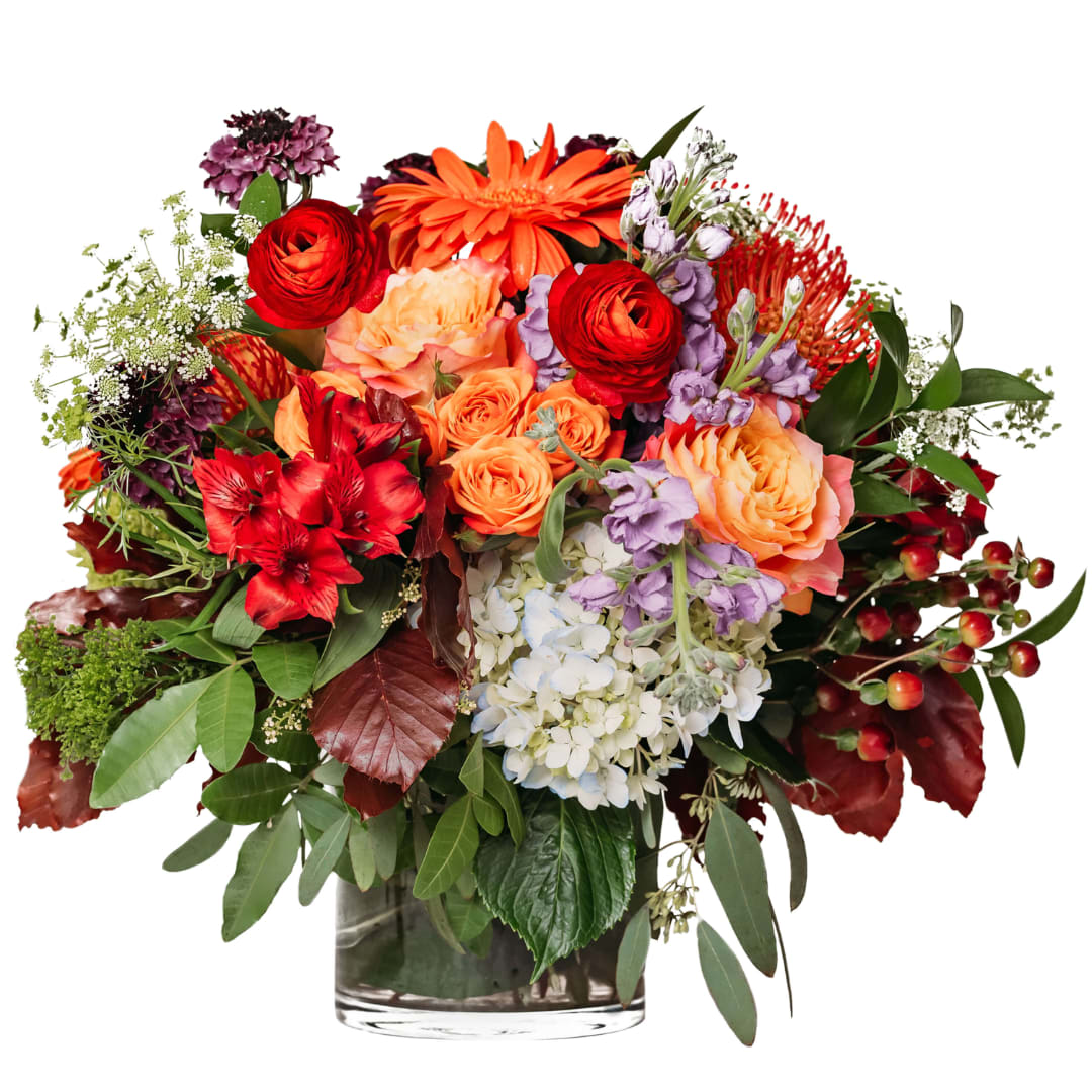 Mixed bouquet of orange, red, purple, and white flowers in a glass vase.