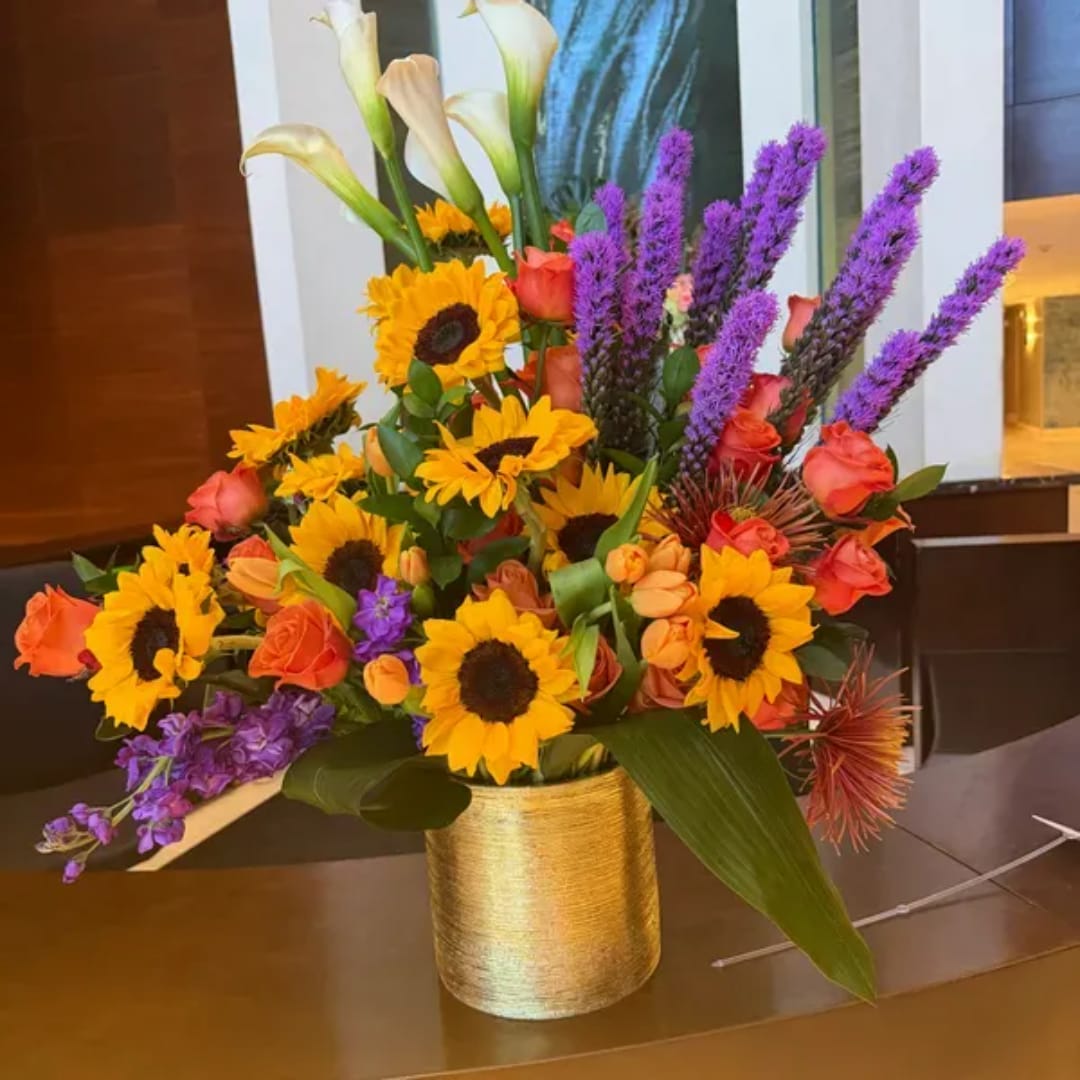 Colorful bouquet of sunflowers, roses, and purple spikes in a gold vase