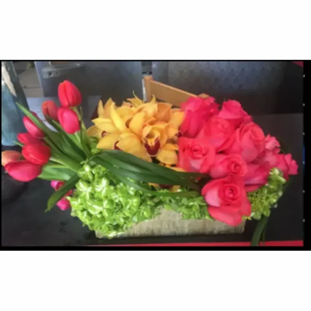 Colorful floral arrangement with tulips, roses, and orchids in a low container