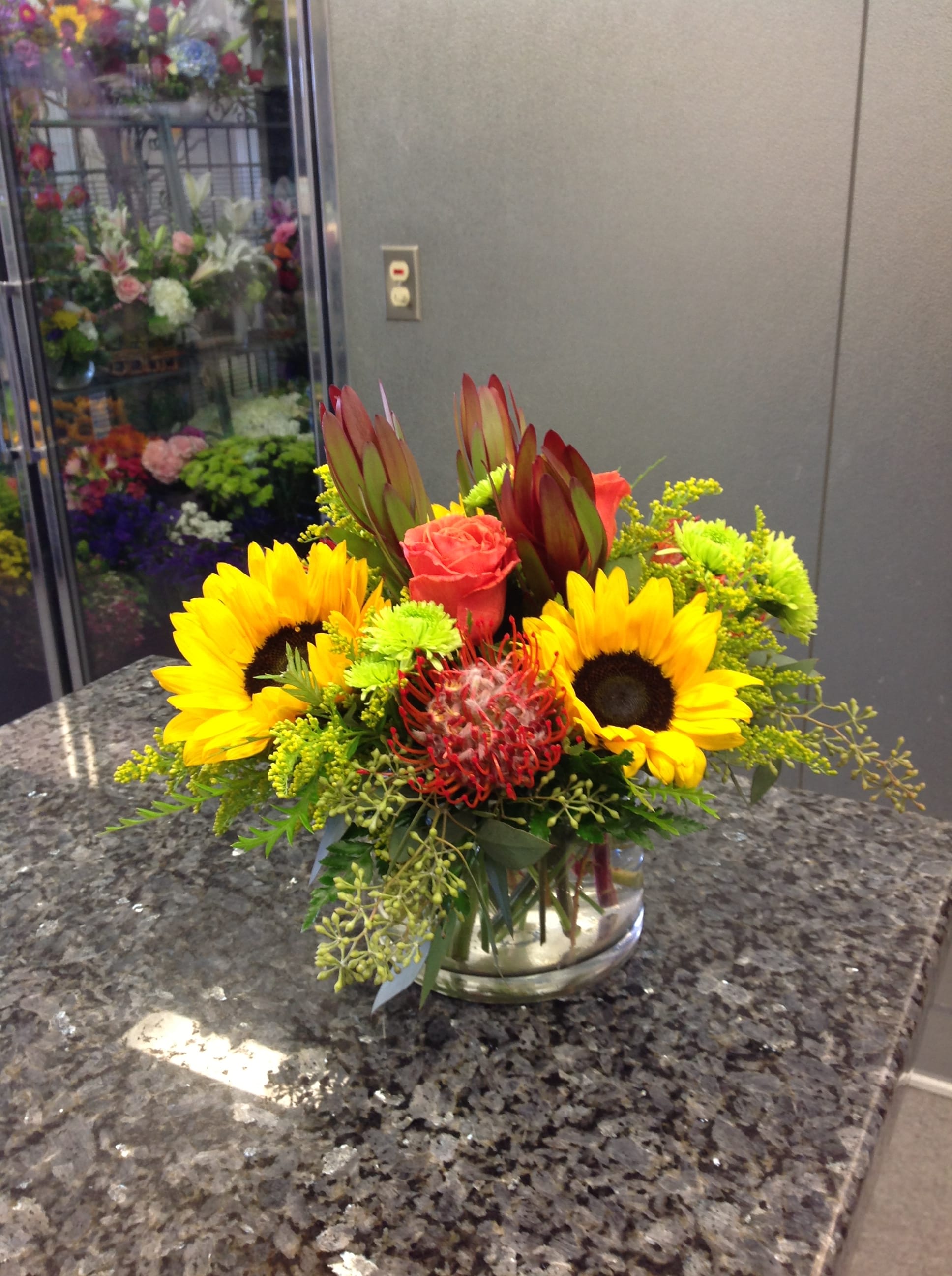 Bright mixed bouquet with sunflowers, roses, and protea in a glass vase