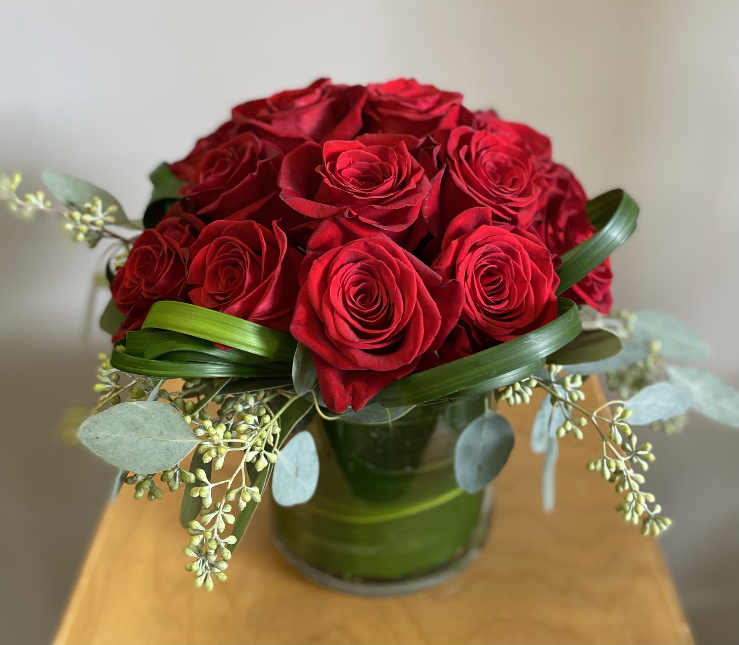 Red roses arranged in a green glass vase with eucalyptus accents
