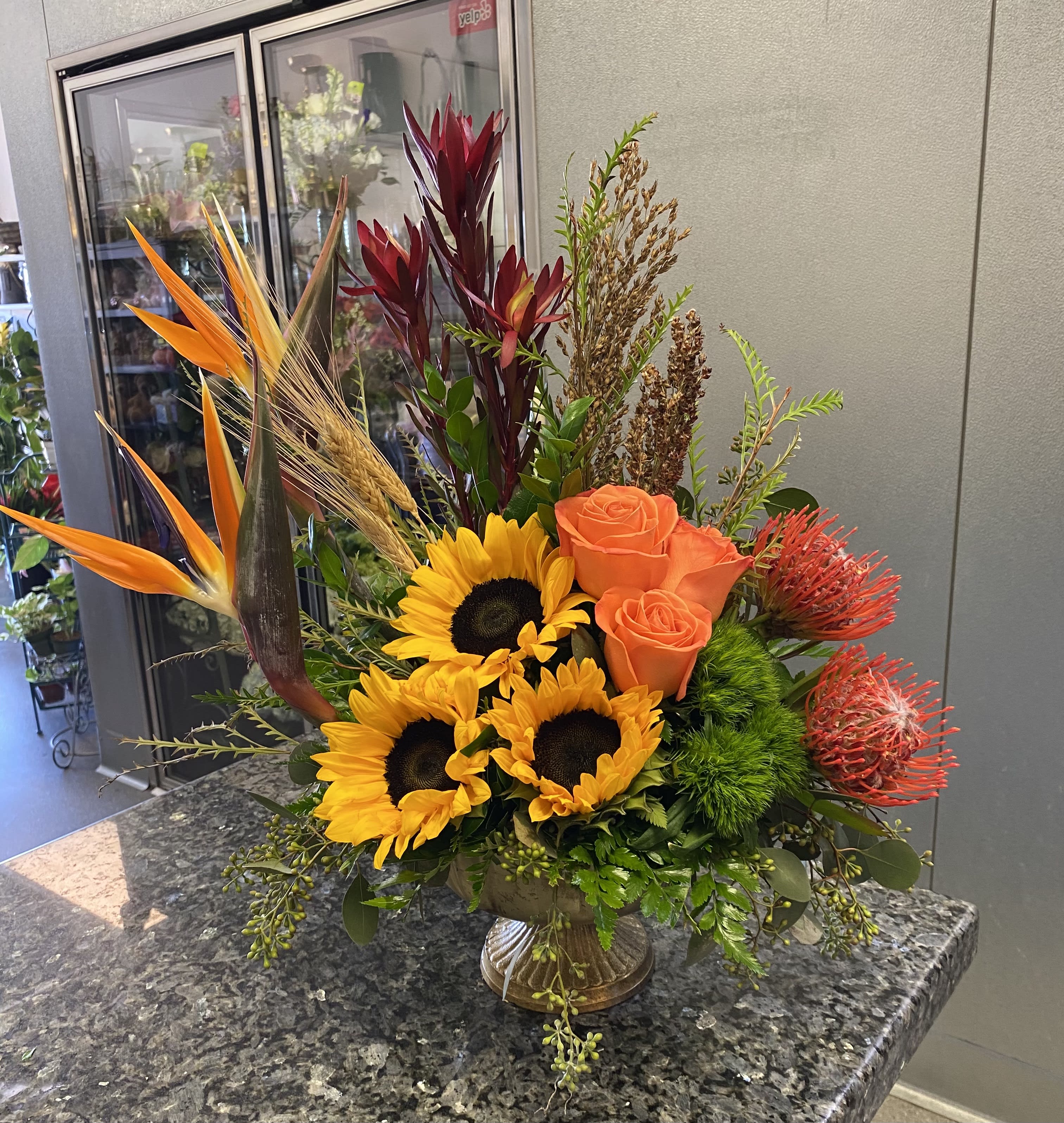 Tropical bouquet with sunflowers, orange roses, and bird of paradise in a vase