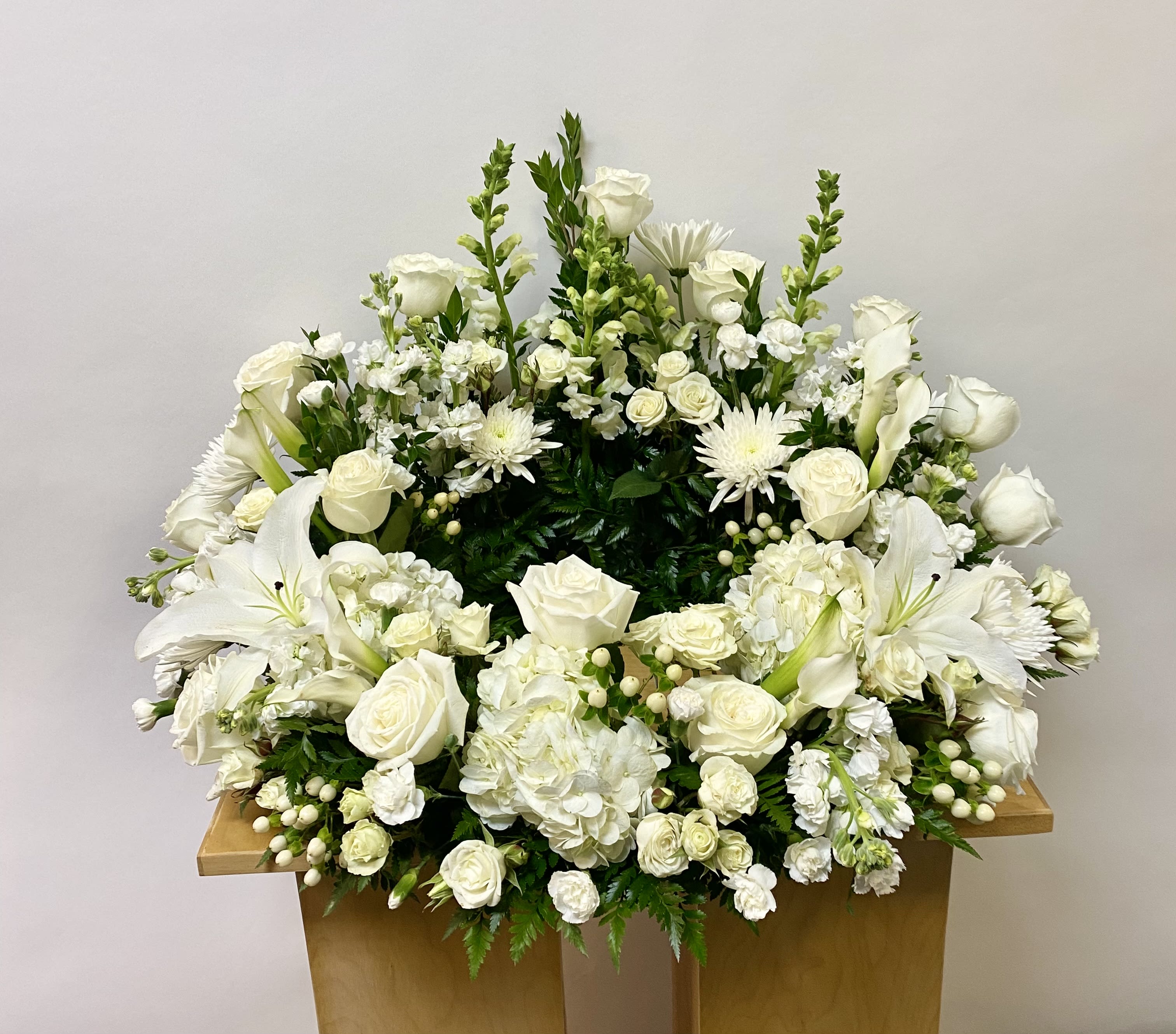 Large white floral arrangement with roses, lilies, and hydrangeas on a wooden stand
