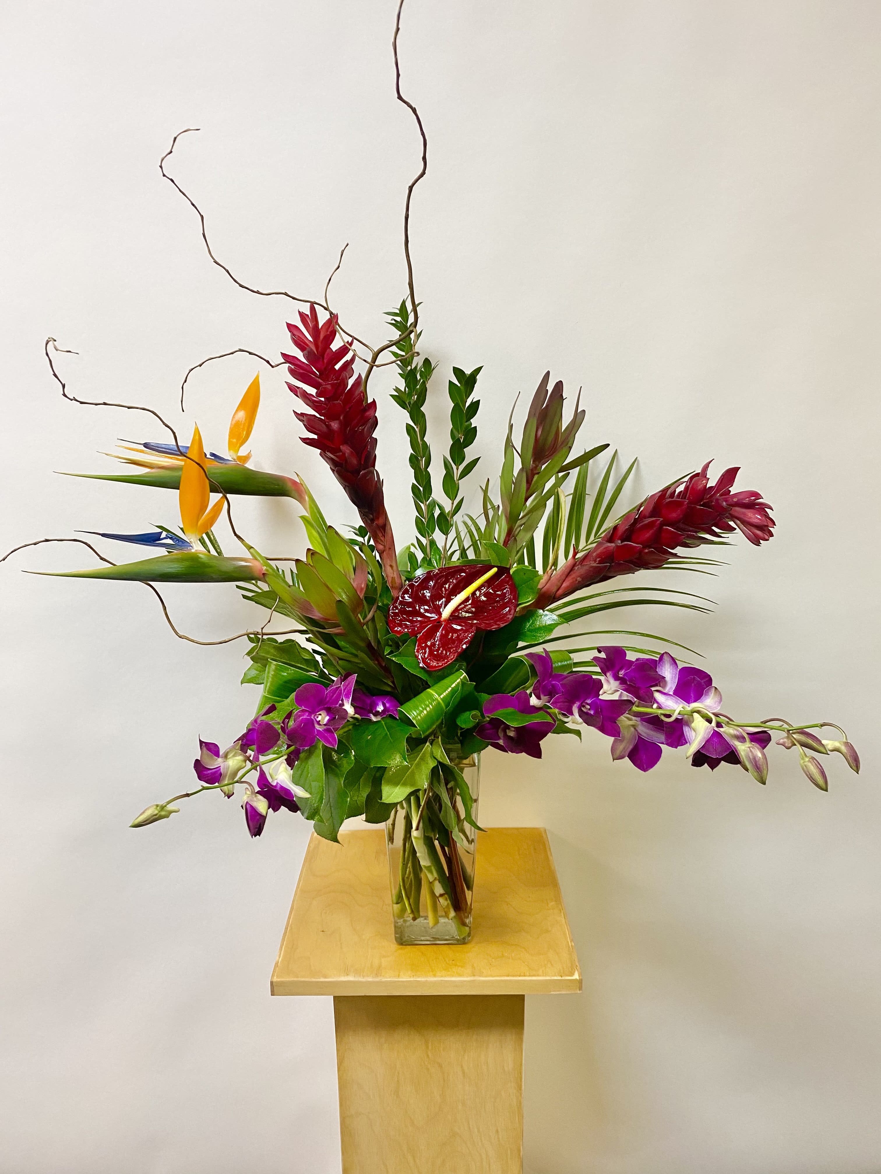Tropical floral arrangement in a glass vase with purple orchids and red anthurium