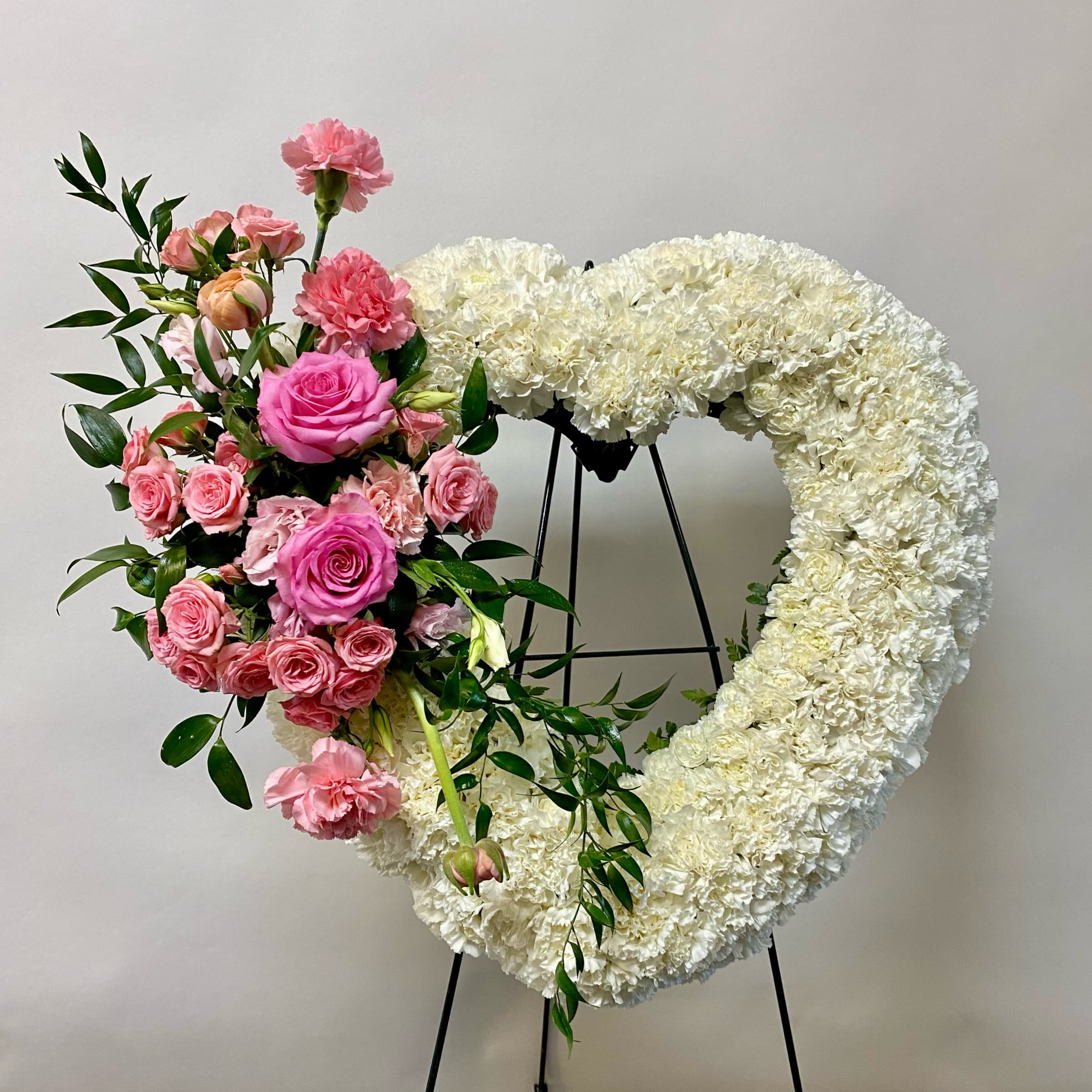 Heart-shaped white floral wreath with pink roses and carnations on a stand