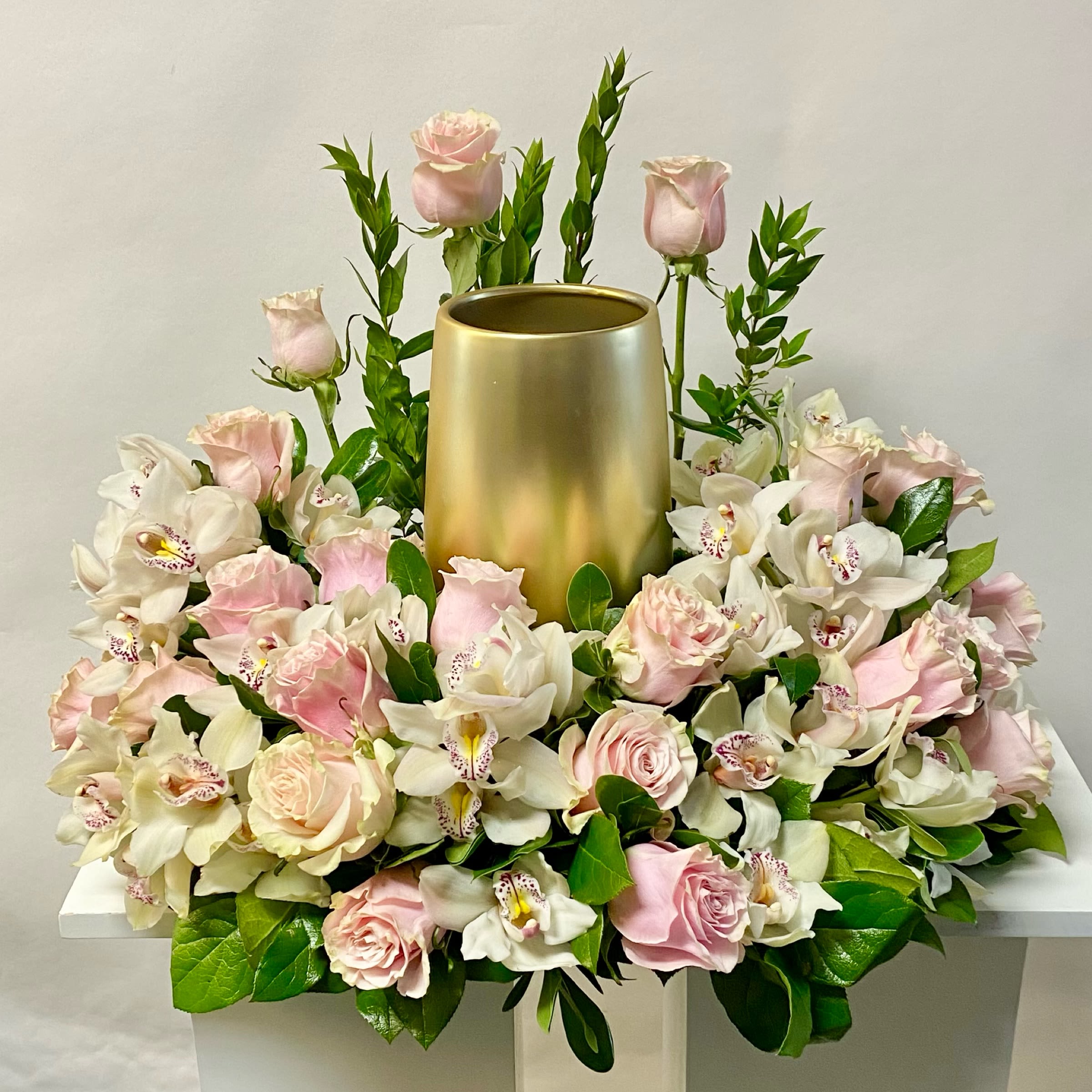 Pink roses and white orchids arranged around a gold cylinder vase