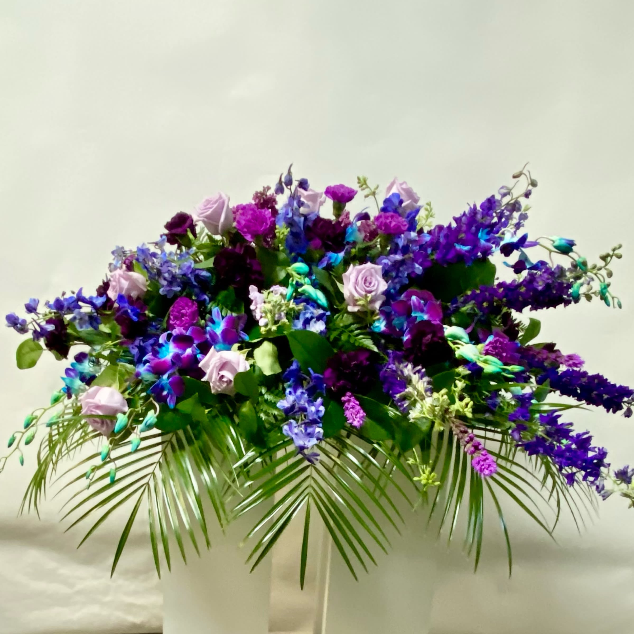 Large purple and blue floral arrangement in a white pedestal vase