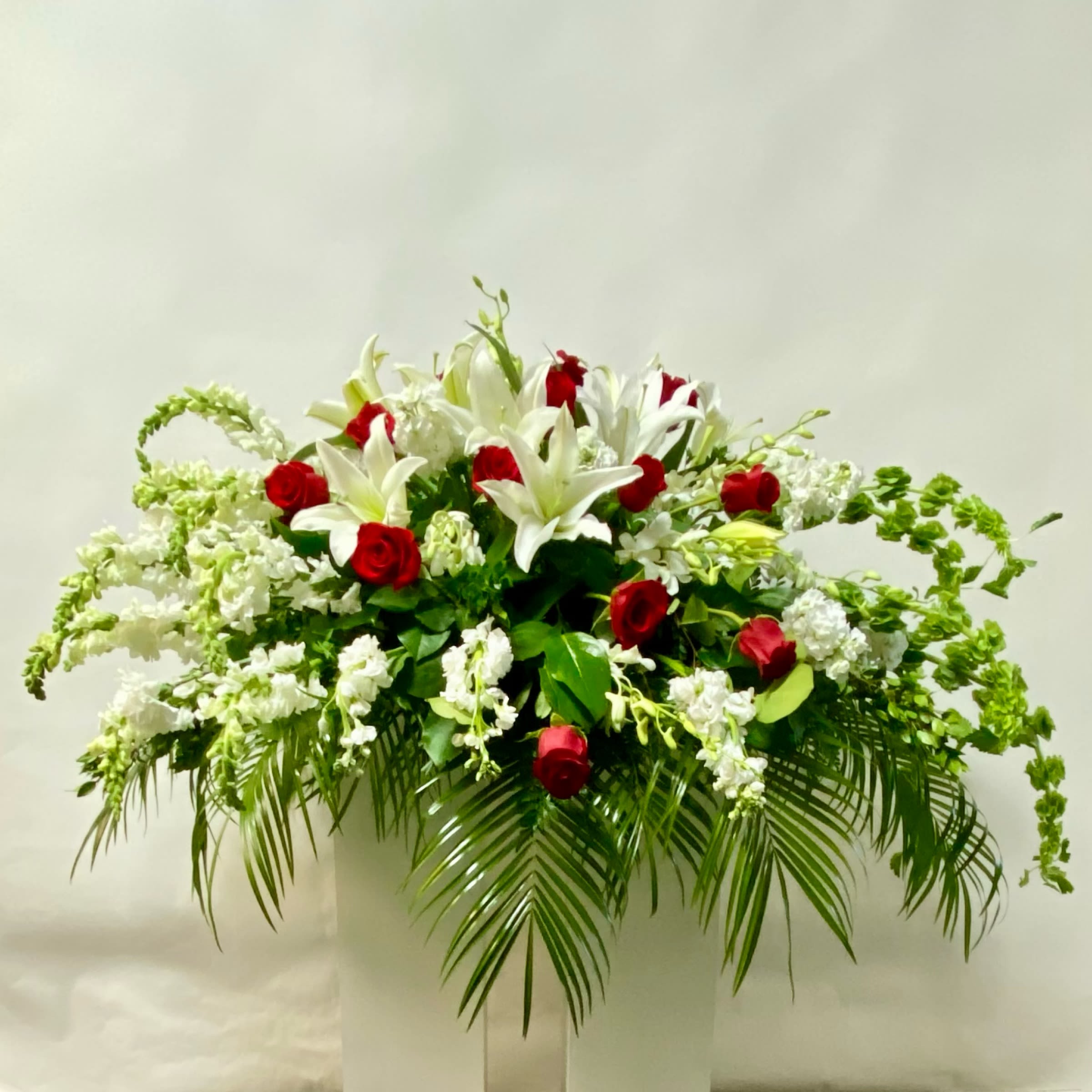 White lilies and red roses in a large arrangement with palm fronds