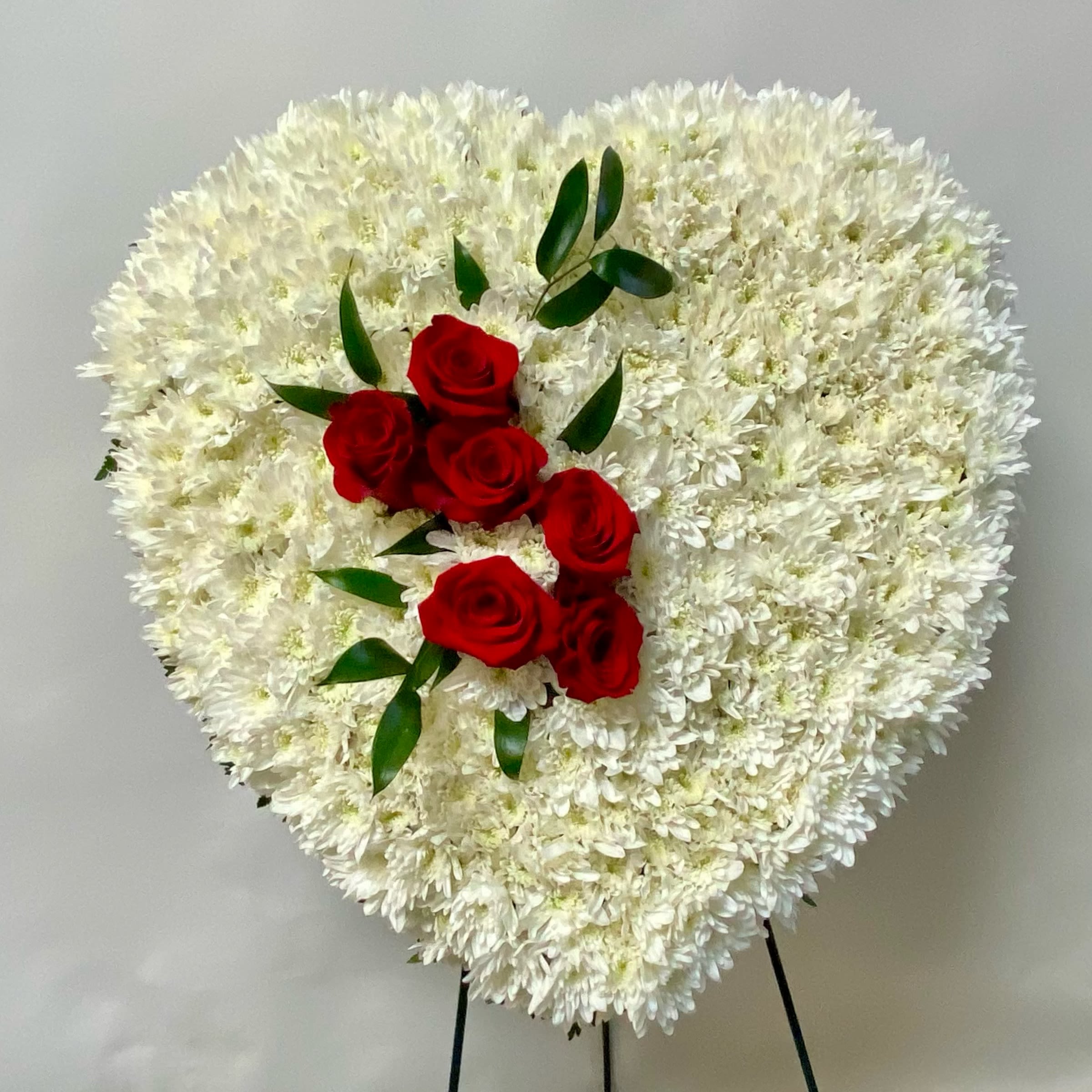 Heart-shaped white floral spray with red roses and greenery