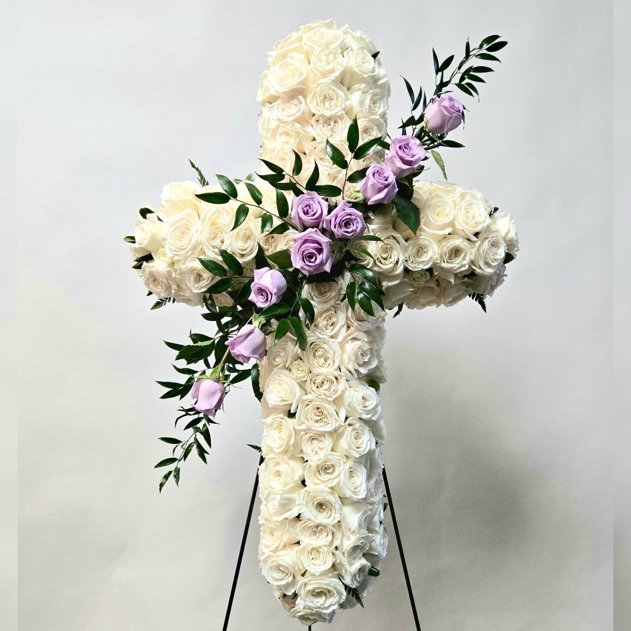White rose cross with lavender roses and greenery on a stand