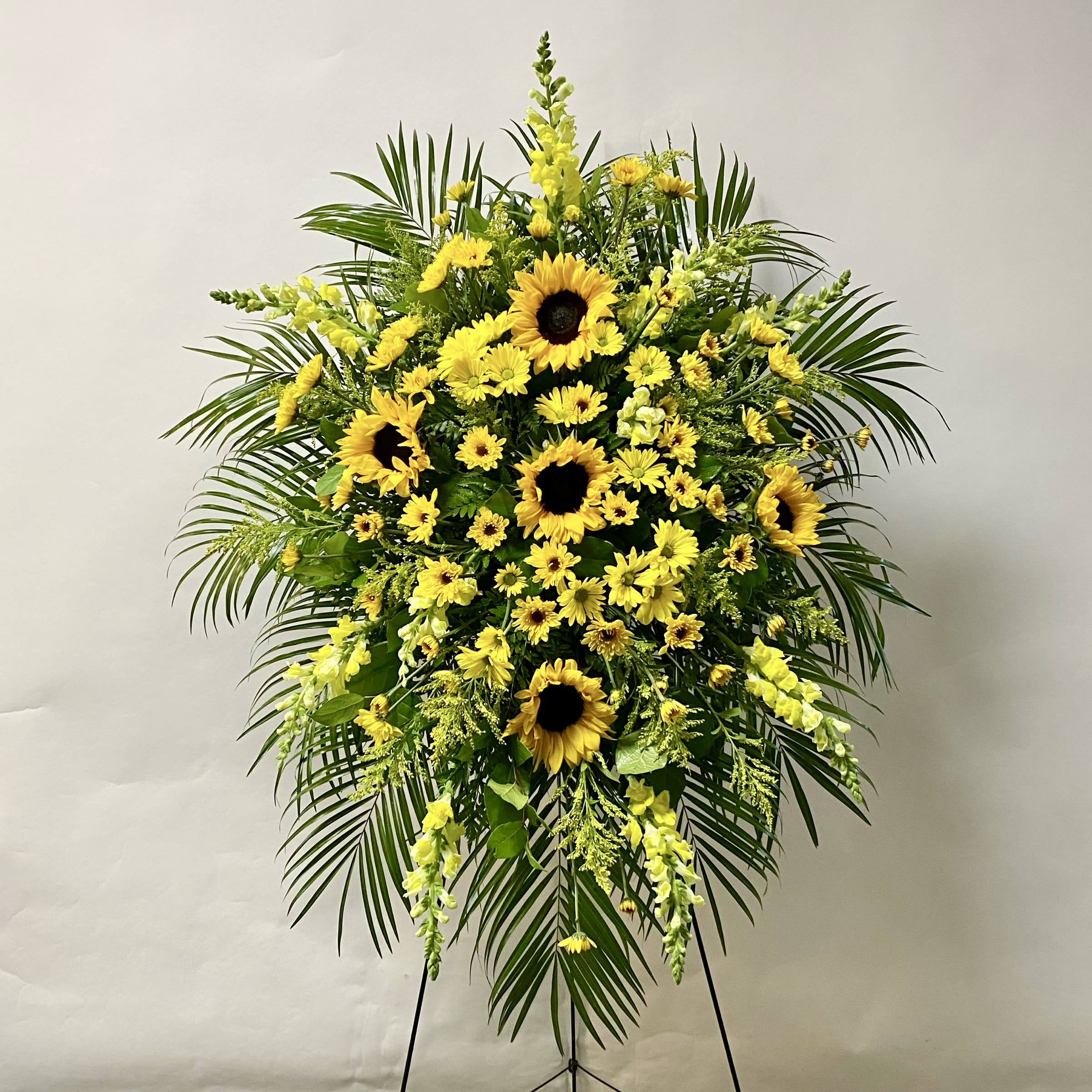 Standing floral spray with yellow sunflowers and daisies on a black easel