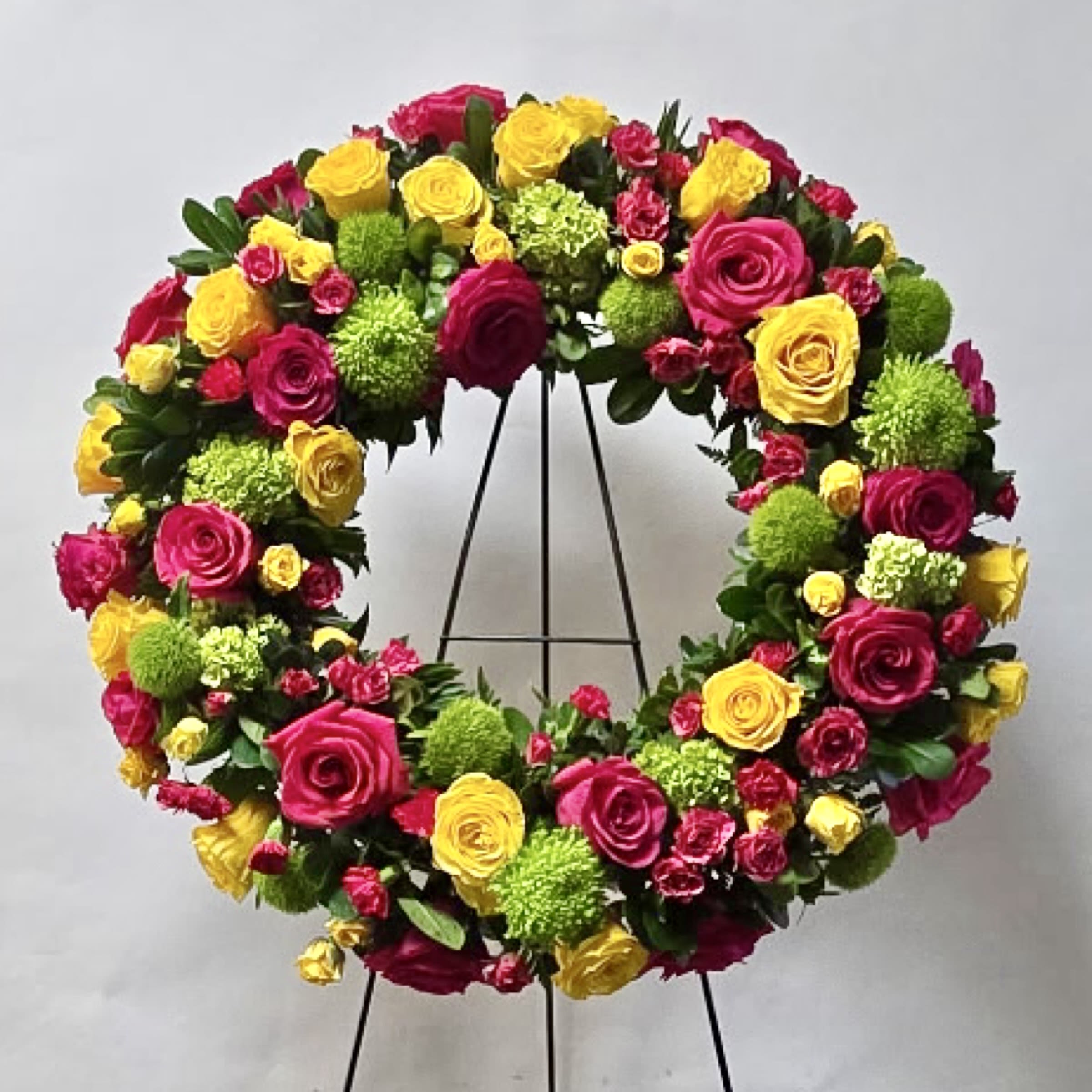 Circular floral wreath of pink and yellow roses on a stand