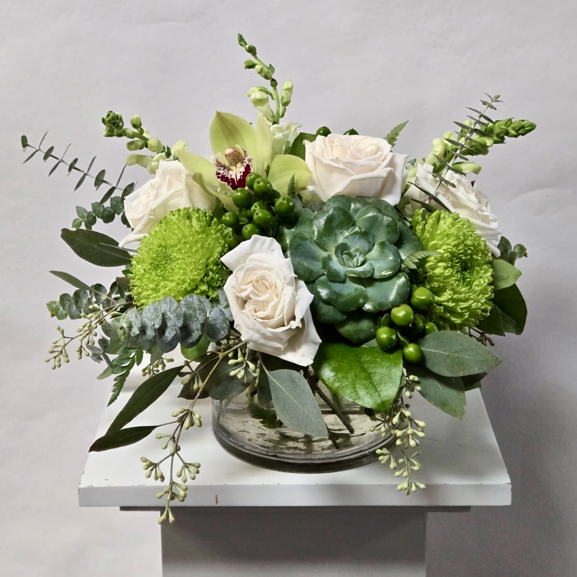 White roses and green blooms arranged in a clear glass bowl.